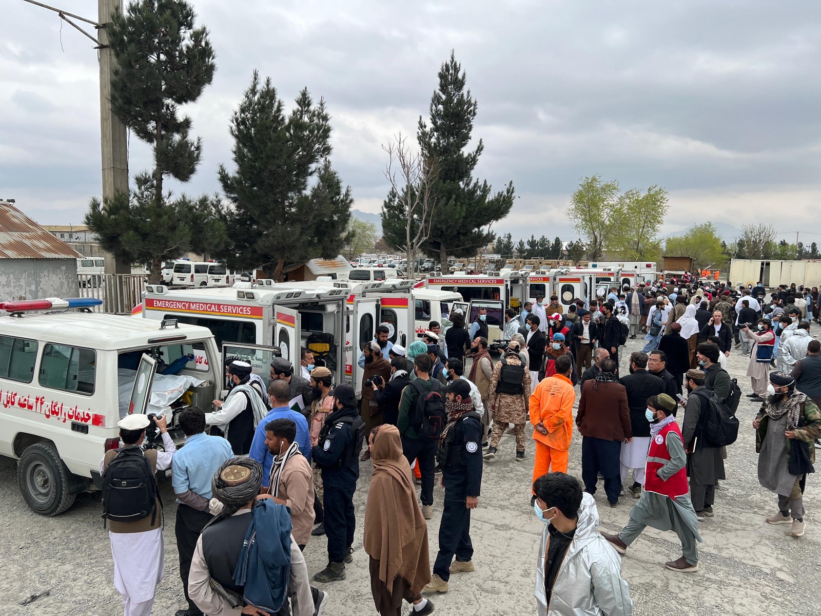 Ambulances and emergency workers gather as people move through a crowded Afghan response scene.