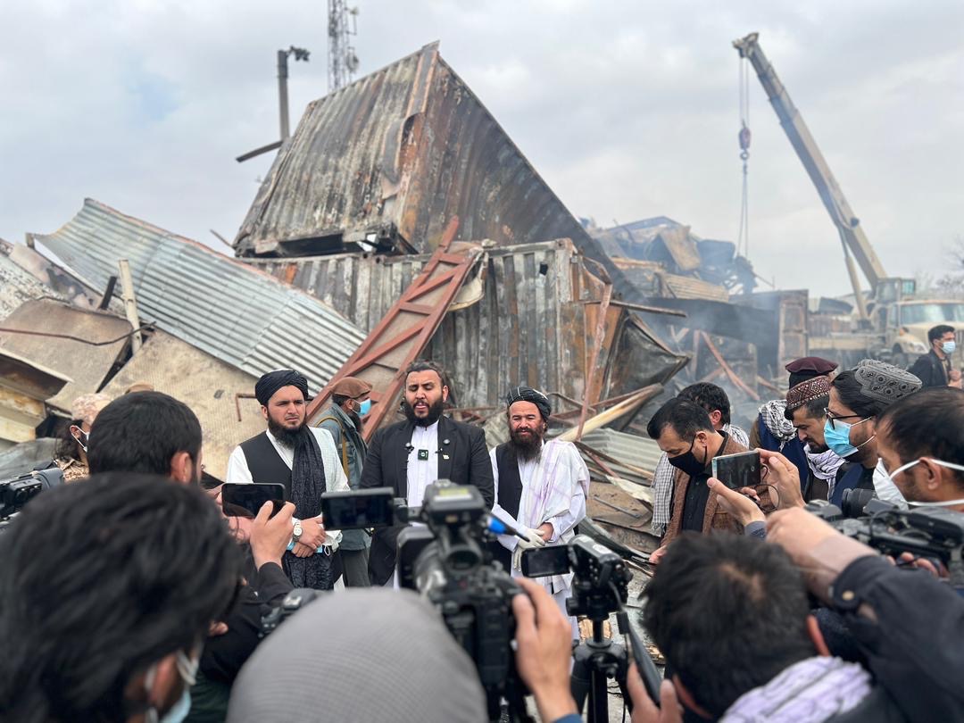 Journalists and officials gather in front of a damaged building at an Afghan strike site.