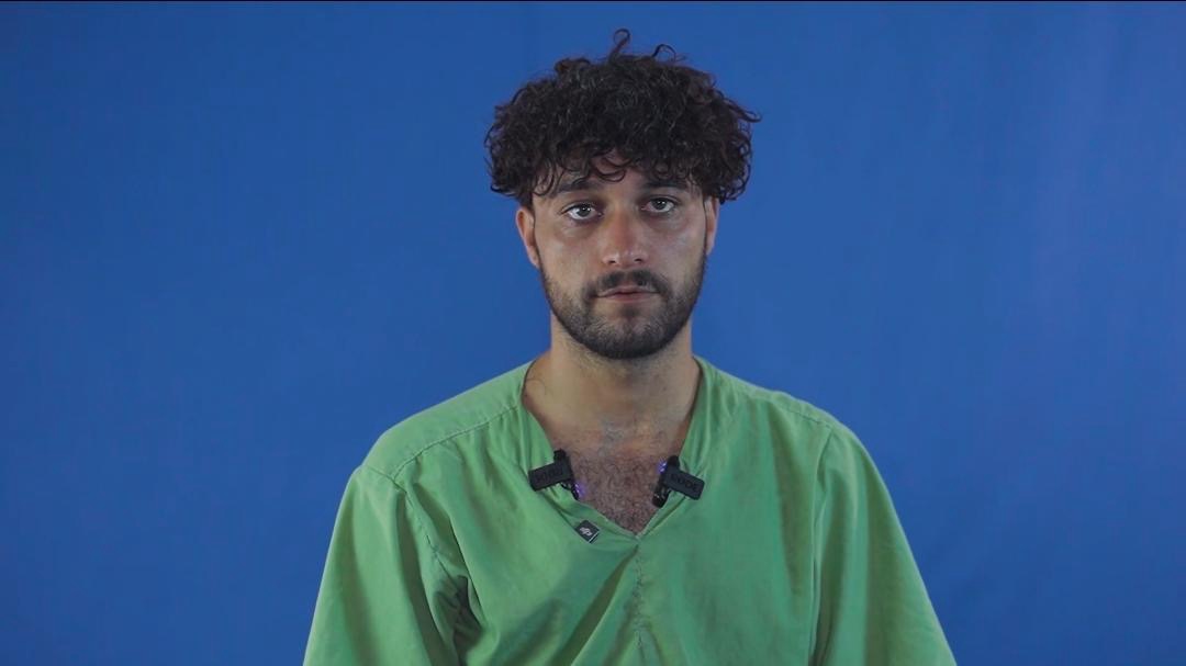 Portrait of Aziz in a green shirt against a blue background, recorded during detention.