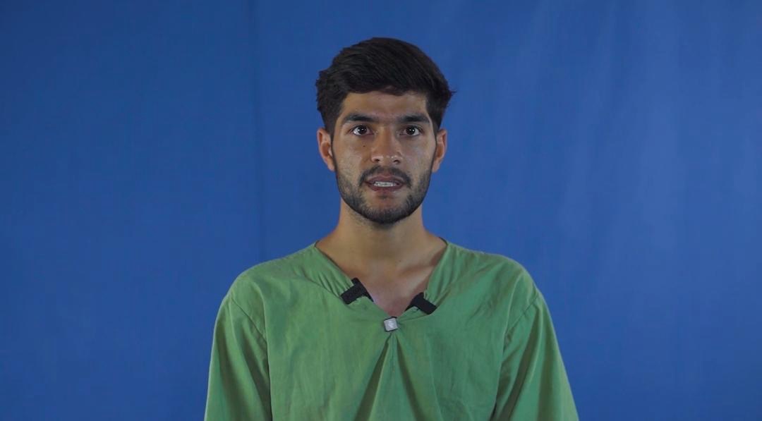 Portrait of Javid in a green shirt against a blue background, recorded during detention.