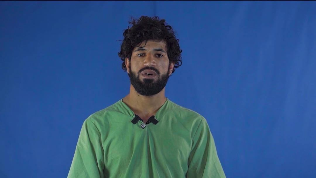Portrait of Nazir Ahmad in a green shirt against a blue background, recorded during detention.
