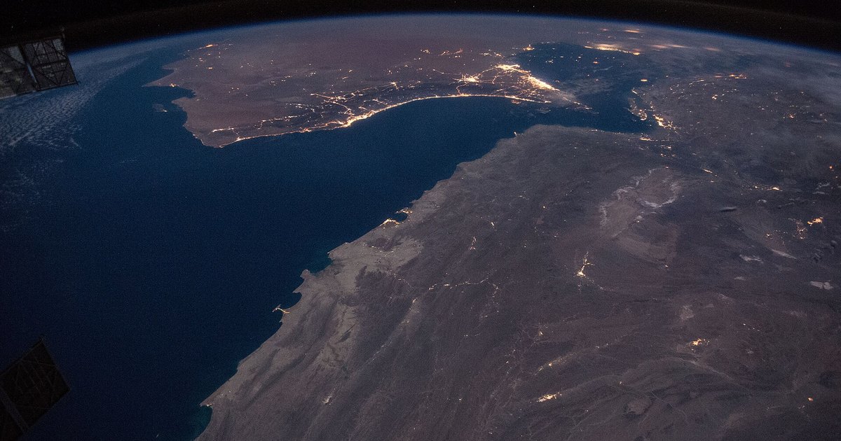 Night-time satellite photograph of the Gulf of Oman and Strait of Hormuz with coastal city lights visible.