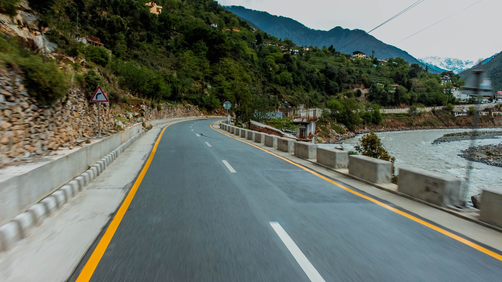 A mountain highway curves beside a river through hills in Khyber Pakhtunkhwa, Pakistan.