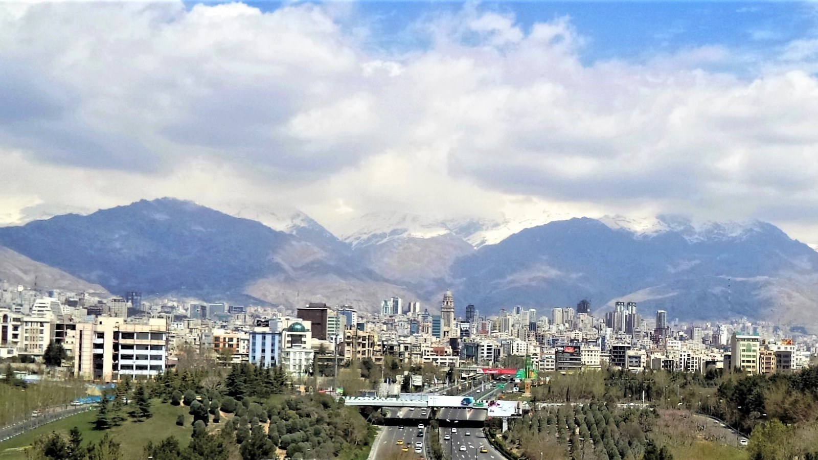 A wide daytime view of central Tehran below snow-capped Alborz Mountains.
