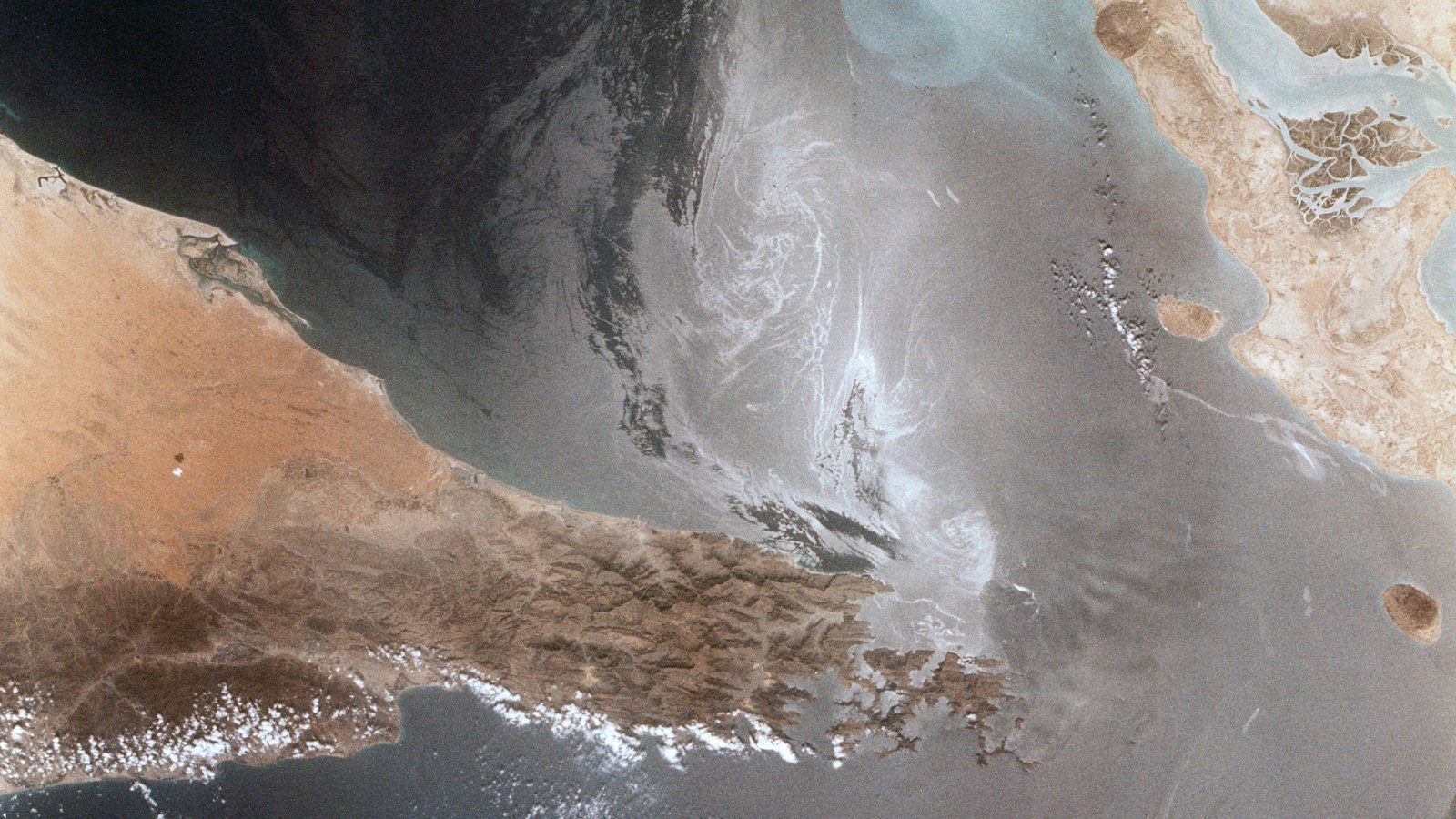 A line of commercial tankers moving through a narrow maritime chokepoint.