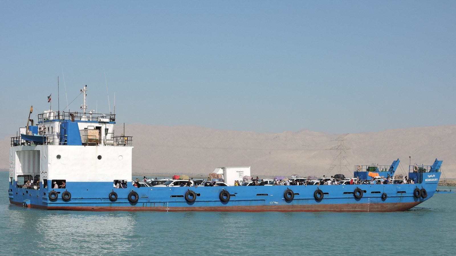 Commercial ships pass through a narrow sea lane under a clear horizon.