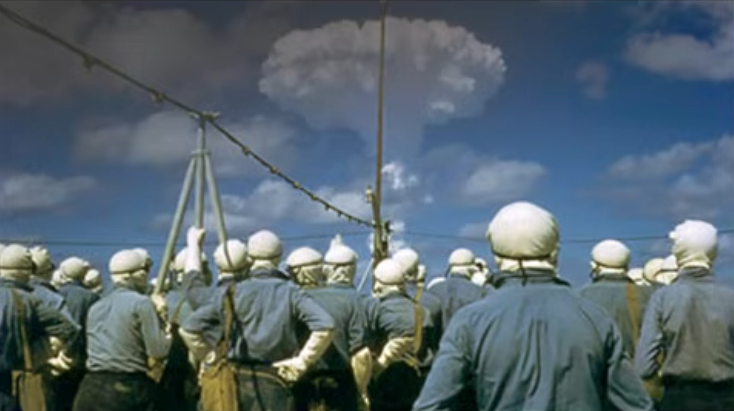 Servicemen observing an atmospheric nuclear test from a distance.
