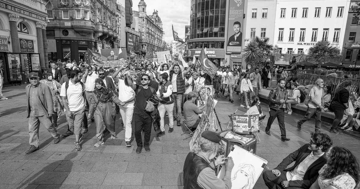A crowd of Imran Khan supporters marching through Leicester Square in London with flags and placards.