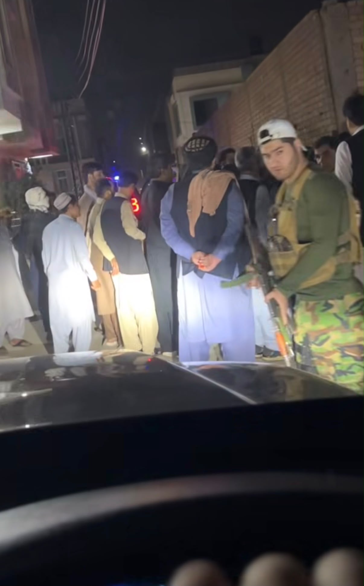 Nighttime video still showing armed men and civilians standing in a street.
