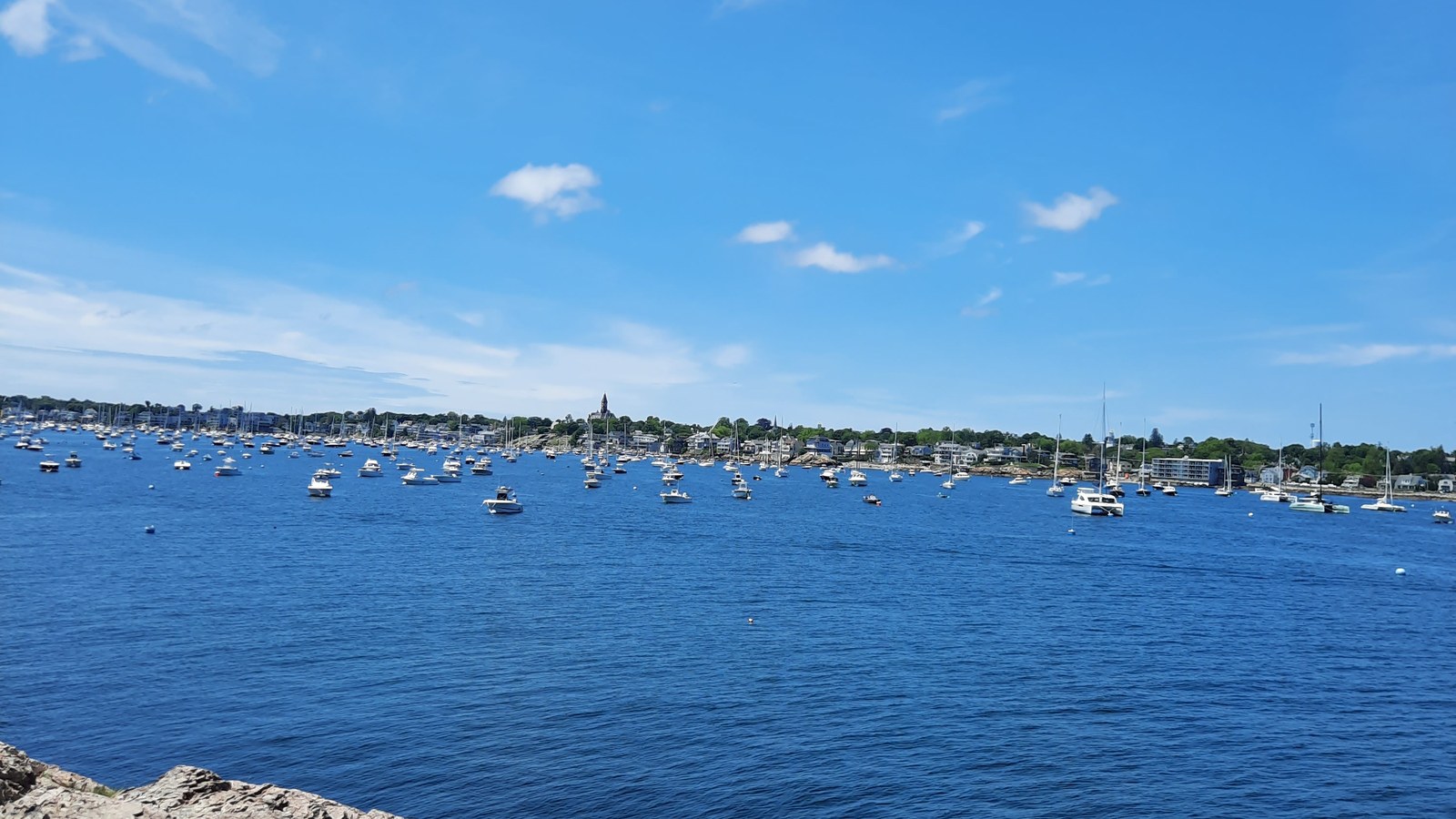 A view of Marblehead Harbor with boats on the water and a rocky shoreline in the foreground
