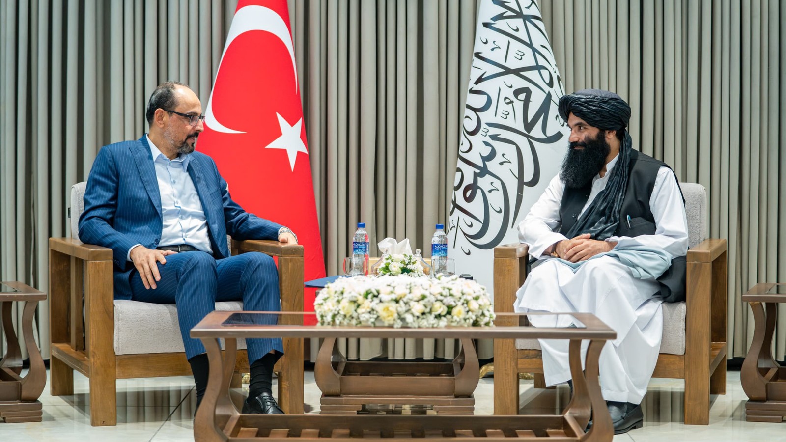 Ibrahim Kalın, head of Türkiye's National Intelligence Organization, seated opposite a Taliban official in Kabul with Turkish and Taliban flags behind them.