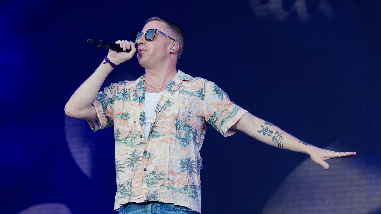 Macklemore performing on stage under bright concert lighting, microphone in hand, at the Festival des Vieilles Charrues in Carhaix, France.